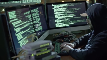 Wall Mural - tracking of hooded man typing on keyboard while working at desk with computer workstation in dark of