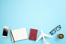 Flat Lay Design Of Work Desk Planning With Plane, Notebook Pencil Passport And Glasses On Blue Background. Travel Concept.