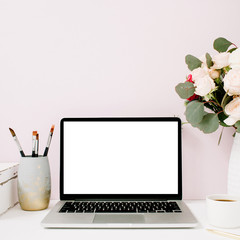 Wall Mural - Home office desk with blank screen laptop, beautiful roses and eucalyptus bouquet, white vintage casket in front of pale pastel pink background. Blog, website or social media concept .