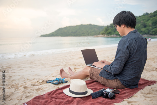 Fotografía Young Asian man working with laptop computer on tropical beach, digital nomad li