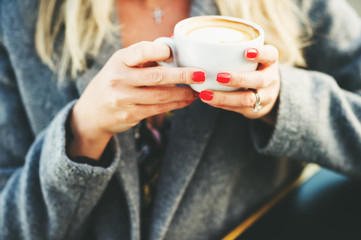 Cup of coffee in woman's hands with bright red manicure