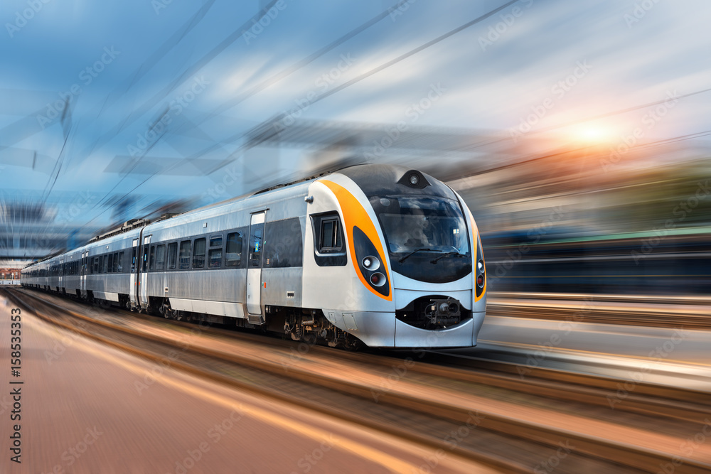 High speed train in motion at the railway station at sunset in Europe. Modern intercity train on the railway platform with motion blur effect. Industrial landscape with passenger train on railroad - obrazy, fototapety, plakaty 
