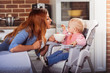 © favorestudio - Little baby girl sits in high chair and feeding with spoon her beautiful mother. Family and motherhood concept. Horizontal