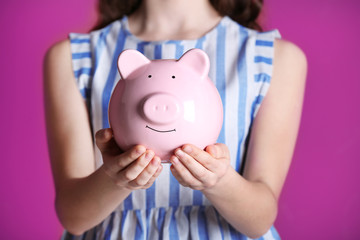 Wall Mural - Young girl holding cute piggy bank in hands on pink background. Saving for education concept