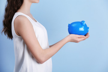 Poster - Young girl holding cute piggy bank in hands on light background. Saving for education concept