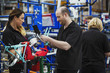© Mint Images - Three cycle factory workers, two women and a man assembling a bicycle in a factory.