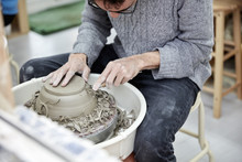 A Man Using A Pottery Wheel, Shaping A Pot Base With A Small Handheld Tool Shaving Off Excess Clay.  
