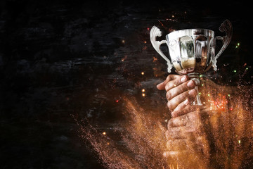 Wall Mural - low key image of a man holding a trophy cup over dark background