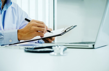 Stethoscope with clipboard and Laptop on desk, Doctor working in hospital writing a prescription, Healthcare and medical concept, test results in background, vintage color, selective focus.