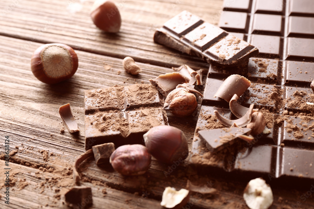 Broken chocolate pieces, nuts and cocoa powder on wooden background