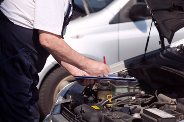 Car or motor mechanic checking a car engine and writing on the clipboard