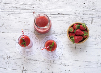 Delicious homemade strawberry smoothie on rustic white wooden background