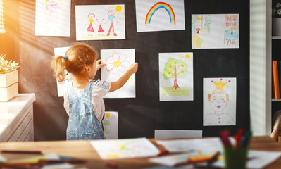 Wall Mural - child girl hanging her drawings on wall.