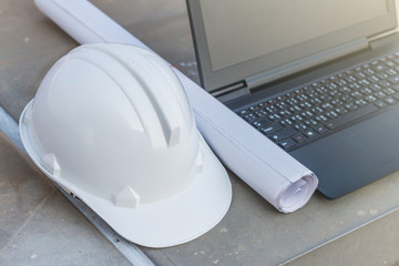 The white safety helmet and the blueprint with laptop at construction site