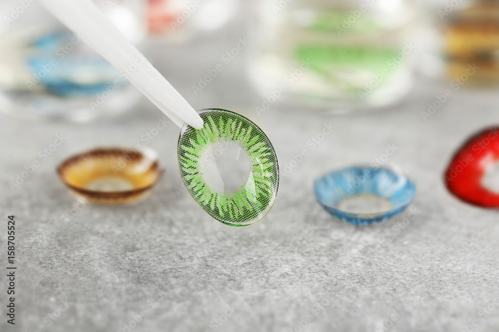 Tweezers holding green contact lens on blurred background