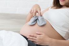 Pregnant Woman Holding Small Baby Shoes In The Bedroom