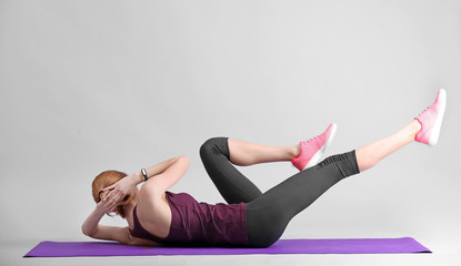 Wall Mural - Beautiful woman doing bicycle crunch on light background