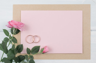 Pink roses and bridal rings with paper greeting card for wedding on background of shabby wooden planks.