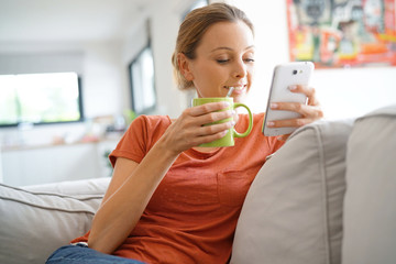 Wall Mural - Woman relaxing in sofa connected with smartphone