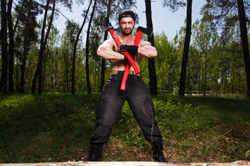 Wall Mural - Strong healthy adult ripped man lumberjack worker standing in the forest with two big crossed axes