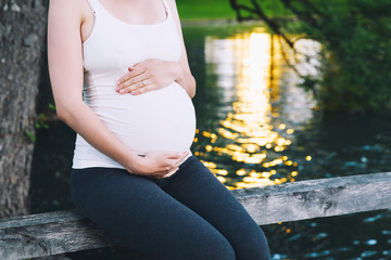 Wall Mural - Pregnant woman holds hands on belly on nature background