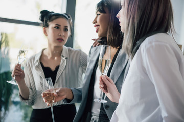 Wall Mural - Professional young businesswoman holding glasses of champagne and talking in office