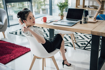 Wall Mural - Attractive young asian businesswoman sitting at table with laptop and looking away