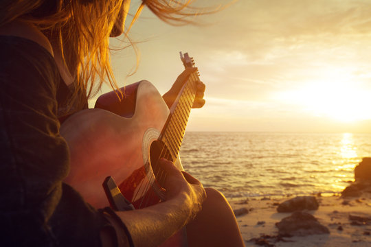 Fototapete - Beautiful young woman playing guitar on sunset beach