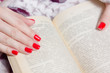 woman manicured hand with red nails and book