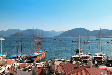 Sea coast: red roofs and yacht bay (marine) in the sunny summer day, blue sky and mountains