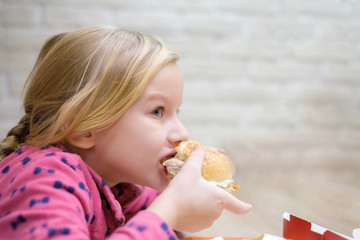 Wall Mural - Adorable girl eat classic burger in fast food restaurant