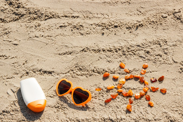 Word and shape of sun, sunglasses with sun lotion, copy space for text on sand at beach