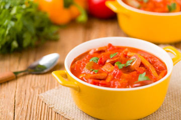 Delicious letcho with fresh vegetables, served in a yellow pot with the fresh bun.