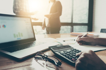 Business team using a calculator and laptop computer to calculate the numbers on his desk in a office.