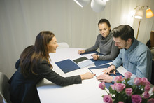 High Angle View Of Mature Female Real Estate Agent Assisting Young Couple With Brochure At Desk In Office