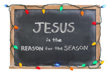 Jesus Is The Reason For The Season Written In White Chalk On A Black Chalkboard Surrounded With Festive Colorful Lights 
Isolated On White