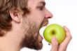 Guy trying to bite big green apple looking at it