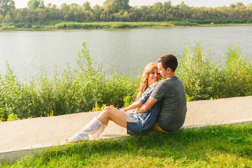 A young couple is romantic in the park on a lake. Man and woman sit in the summer sun in the green grass