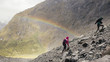 © HOWL/Stocksy - A couple of hikers climbs a rocky mountain with a rainbow in the background