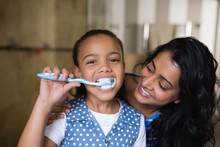Portrait Of Girl Brushing Teeth With Mother In Bathroom
