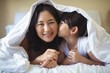 © wavebreak3 - Daughter kissing her mother under blanket in bedroom