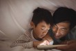 © wavebreak3 - Father and son using digital tablet under blanket in bedroom