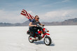 © Jesse Morrow/Stocksy - portrait of young male wearing american flag while riding motorcycle through desert salt flat