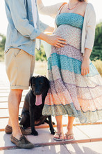 Closeup Of Young Pregnant Couple Standing With Their Black Dog On The Beach Promenade
