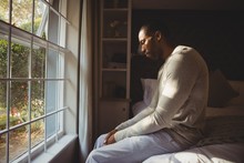 Side View Of Sad Man Sitting On Bed By Window