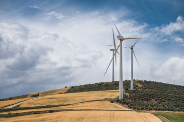 Three windmills on a hill with cloudy sky in the background. Renewable energy generation.