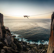 © Micky Wiswedel/Stocksy - man lying on a tightrope highline between two cliffs overlooking the sea at sunset