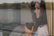 © Jovo Jovanovic/Stocksy - Woman looking through window and holding her tea