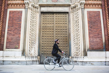 Young Man Riding A Bicycle In Front Of An Ancient Neo-Gothic Church