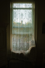 Woman Sits Behind A Lace Curtain At A Window Lost In Her Own Thoughts